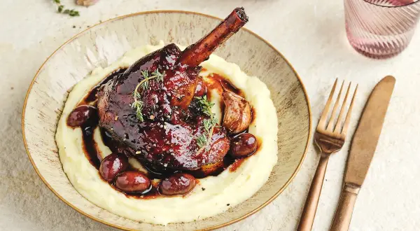 Une souris d'agneau braisée, nappée d'une sauce foncée, servie sur une purée onctueuse avec des olives et de l'ail rôti.