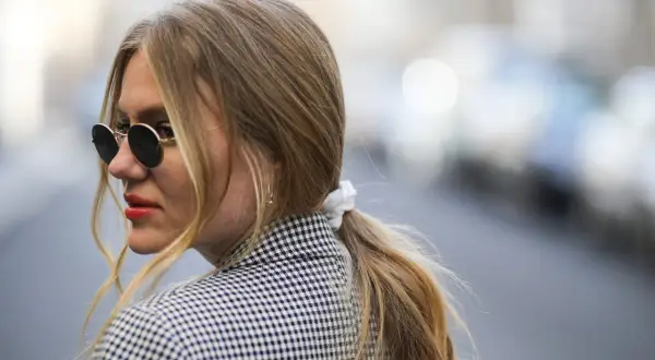 Kobieta w okularach przeciwsłonecznych i marynarce w kratkę, z blond kucykiem.