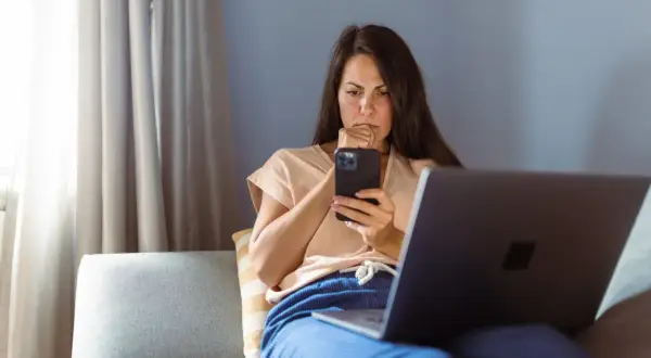 Besorgte Frau am Handy, die über eine neue Betrugsmasche Immobilien recherchiert.