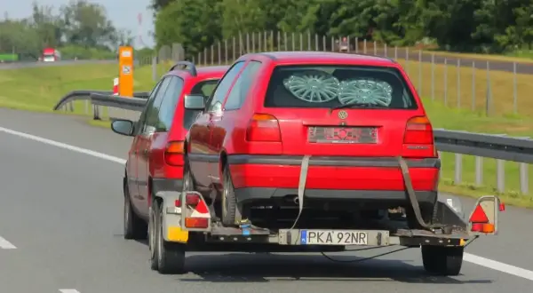 Czerwony Volkswagen Golf na lawecie, holowany przez inny samochód. To dowód, że automatem można holować inne auto, choć nie jest to standardowa sytuacja.