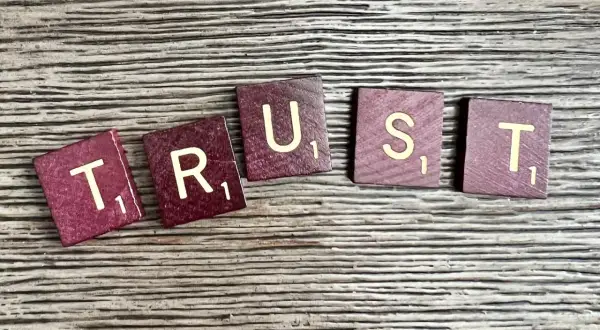 Litery "TRUST" ułożone na drewnianym tle. Brak zaufania w związku czy to ma sens?