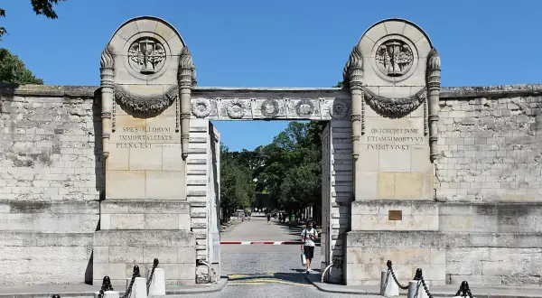 Monumentalna brama cmentarza Père Lachaise z łacińskimi inskrypcjami i płonącymi pochodniami.