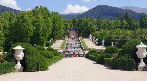 Jardín de la Granja de San Ildefonso, Madrid. Escalera de agua con estatuas y fuentes, rodeada de vegetación y montañas.