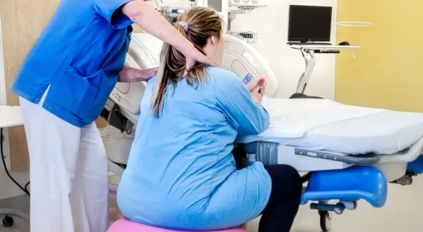 Barnmorska stöttar en kvinna i gravid vecka 36 som sitter på en rosa boll vid en förlossningssäng.