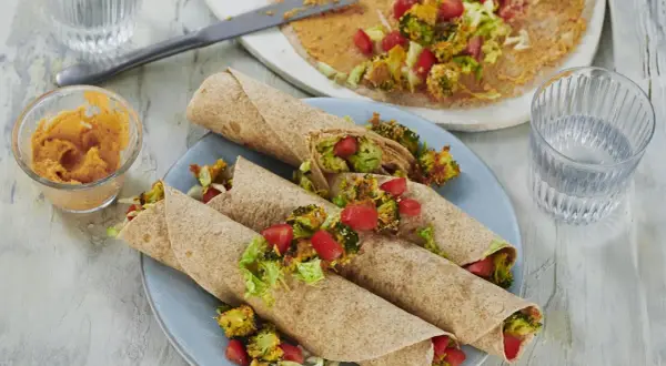 Leckere wraps vegetarisch gefüllt mit geröstetem Brokkoli, Tomaten und Salat. Dazu ein Dip und ein Glas Wasser.