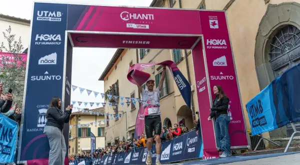 Un coureur franchit la ligne d'arrivée du Chianti by UTMB, acclamé par la foule. Il tient une banderole rose de finisher.
