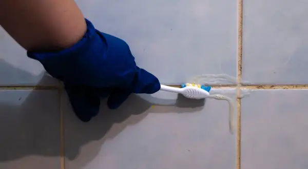 Main bleue, brosse à dents et produit nettoyant pour lutter contre la moisissure joint salle de bain.