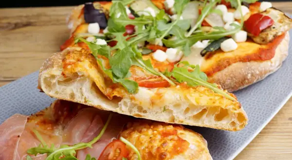 En romersk pizza med krispig botten, toppad med ruccola, tomater och mozzarella. En annan bit visar prosciutto och färska örter.