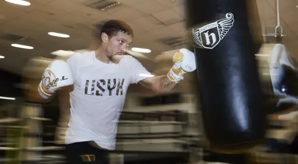 A boxer in a white t-shirt and gloves trains intensely during a boxing training camp, punching a heavy bag.