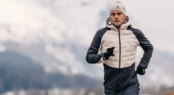 Un homme court par temps froid, portant une veste pour courir l'hiver, un bonnet et des gants.
