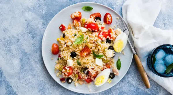 Un piatto colorato di insalata di riso con pomodorini, olive, mozzarella e uova sode. Perfetta per un pasto estivo.