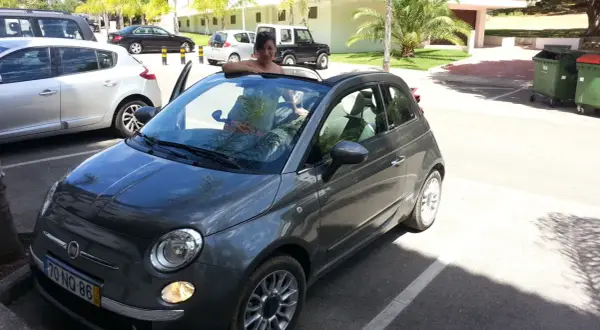 Frau lehnt sich aus einem grauen Fiat 500 Cabrio, bereit für eine Spritztour. Gute mietwagen portugal tipps für den Urlaub!