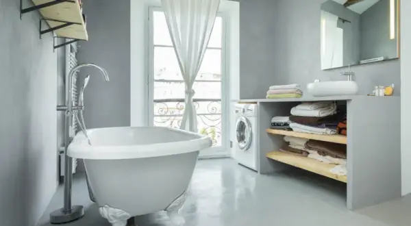 Un baño moderno con bañera independiente, lavadora y estantes con toallas. La idea de pintar bañera aquí es para un estilo minimalista.