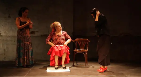 Tres mujeres en escena. Una sentada, con falda roja y blusa estampada, como **la Chana**. Otra de pie, con vestido largo y estampado. La tercera, de negro, con el pelo recogido.