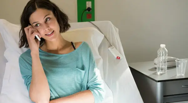 Kobieta w szpitalnym łóżku rozmawia przez telefon, szukając informacji, co niszczy raka.