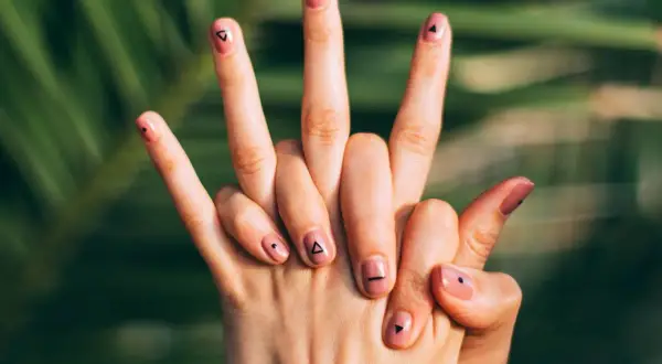Manos con uñas flamencas en tono rosa pálido, decoradas con pequeños triángulos y puntos negros.