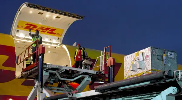 Pracownicy rozładowują samolot DHL. Z jakiego kraju pochodzi ten transport?