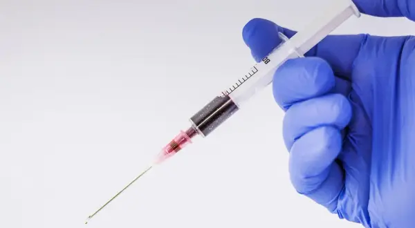 Ręka w niebieskiej rękawiczce trzyma strzykawkę z ciemnym płynem. Jak leczyć hemofobię? Terapia może obejmować psychoterapię.