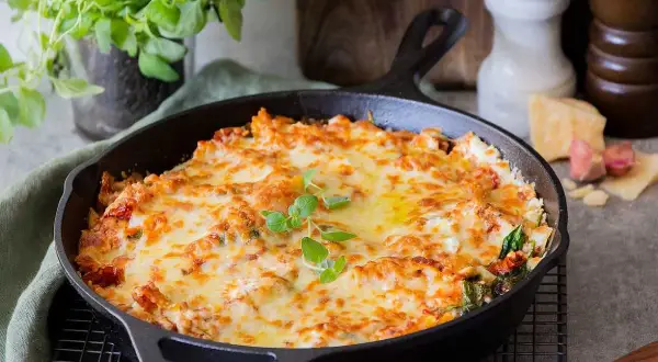 En gyllene, bubblande vegetarisk lasagne i gjutjärnspanna, toppad med färska örter. Perfekt för en mysig middag.
