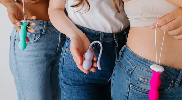 Trois femmes en jeans tiennent des dispositifs pour le biofeedback périnée : un vert, un violet et un rose.