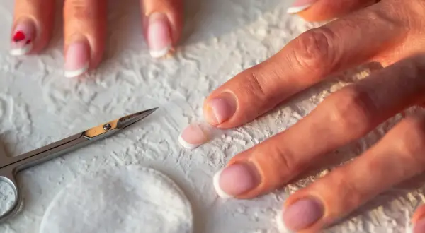 Dłonie z francuskim manicure, nożyczki i wacik. Zastanawiasz się, dlaczego nie rosną paznokcie u rąk? Może to kwestia pielęgnacji.