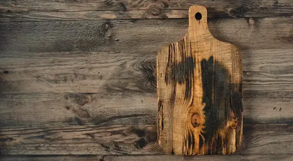 Planche à découper en bois brut, brûlée et texturée, sur un fond de planches de bois vieilles. Idéal pour apprendre comment traiter une planche de bois brut.