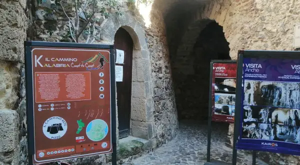 Cartello informativo sul Cammino Calabria Coast to Coast, con scorci di antiche costruzioni in pietra.