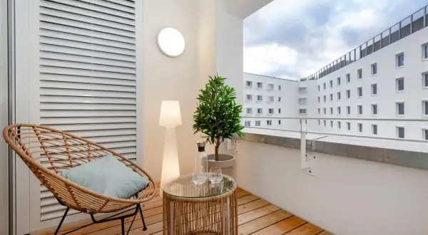 Gemütlicher Balkon mit Holz-Bodenbelag, ideal für eine Mietwohnung. Ein Rattansessel lädt zum Entspannen ein.