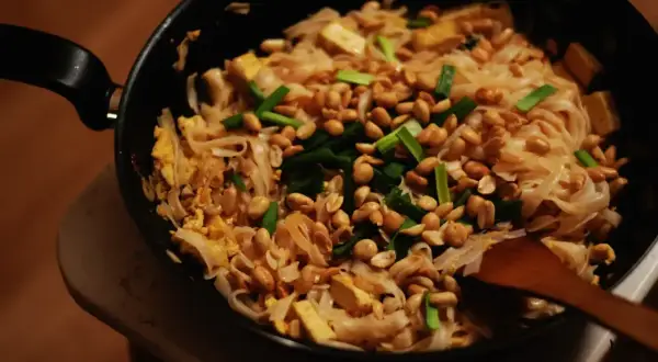 Pyszny sos pad thai z makaronem ryżowym, tofu, orzeszkami ziemnymi i szczypiorkiem, przygotowywany na patelni.