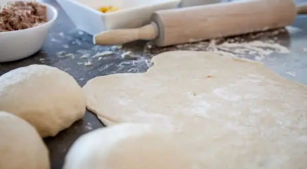 Pizzateig, Nudelhölzer und Schüsseln mit Zutaten auf einer Arbeitsfläche.