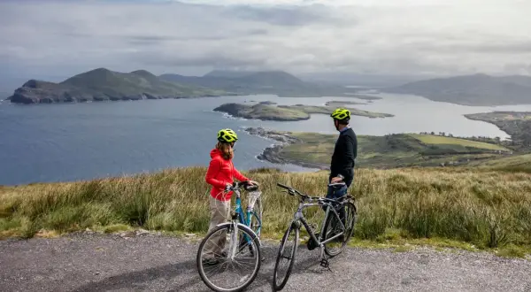 Pareja disfrutando de un paseo en bicicleta por la costa de Irlanda, con vistas a islas y montañas.