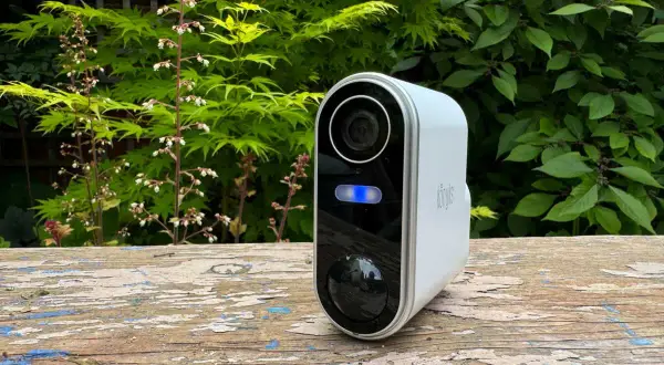 Une caméra de surveillance blanche avec une lumière bleue allumée, posée sur un banc en bois. Un moyen simple pour savoir si une caméra fonctionne.