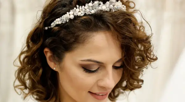 Brautfrisur kurze Haare Bob mit funkelndem Diadem. Lockige Haare umrahmen das Gesicht einer lächelnden Braut.