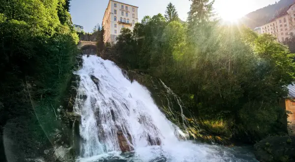 Tosender Wasserfall stürzt durch grüne Hänge in Bad Gastein Altstadt, wo sich ein imposantes Hotel über dem Naturschauspiel erhebt.
