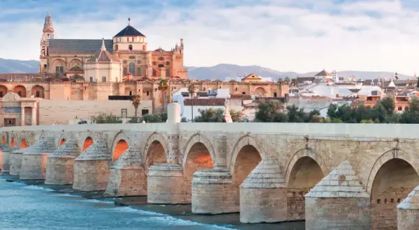 El Puente Romano cruza el Guadalquivir hacia la impresionante mezquita catedral de Córdoba, bañada por la luz del amanecer.