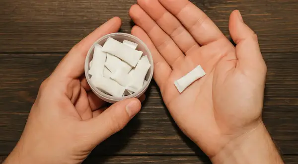 Dłonie trzymające pojemnik z białymi woreczkami nikotynowymi i jeden woreczek w dłoni. Czy snus jest legalny w Polsce?