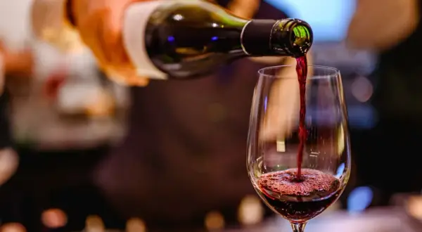 Ciemnoczerwone bordeaux wino leje się z butelki do kieliszka, tworząc piankę.