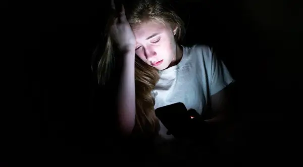 En tonåring med handen mot pannan, upplyst av en mobilskärm. Känslan av depression hos barn kan testas genom att observera sådana här stunder.