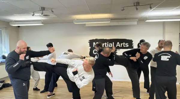 Män tränar wing chun i en lokal. En man utför en hög spark medan andra övar försvar.