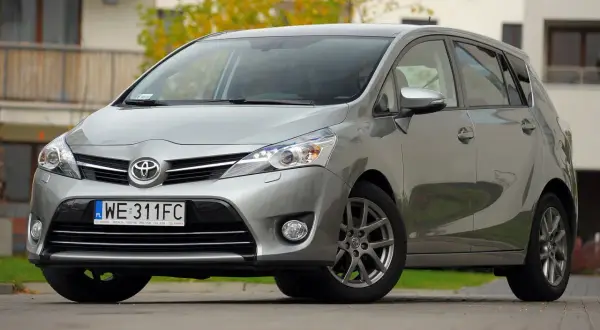 Srebrna Toyota Verso 1.8 benzyna zaparkowana przed budynkiem.