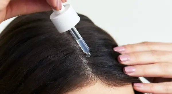 Eine Pipette mit Serum tropft auf die Kopfhaut, um das Haarwachstum mit Retinol zu fördern.