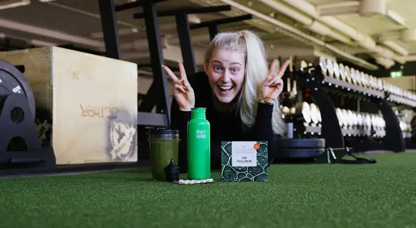 Glad kvinna med energi i gymmet, redo att ta sig an dagen. Frågan är: hur blir man pigg? Kanske med en grön smoothie och kosttillskott?