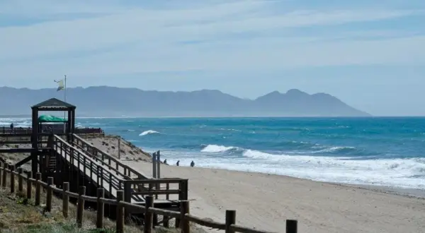 Un día perfecto para un paseo marítimo en Retamar. La arena dorada, el mar azul y las montañas de fondo crean un paisaje idílico.