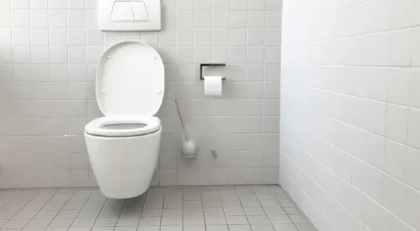 Bagno bianco con WC aperto. Si nota una piccola macchia d'acqua sul pavimento, forse il galleggiante wc perde acqua.