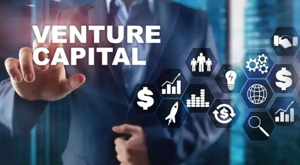 Biznesmen wskazuje na ekran z napisem VENTURE CAPITAL i ikonami symbolizującymi rozwój, pieniądze i innowacje.