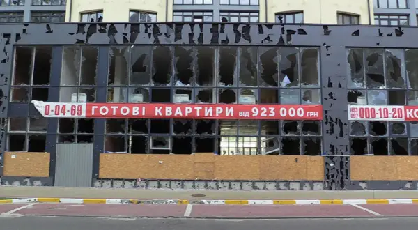 Uszkodzony budynek z banerem "GOTOWI KWARTRYRY від 923 000 ГРН". Zastanawiasz się, ile kosztuje mieszkanie na Ukrainie?
