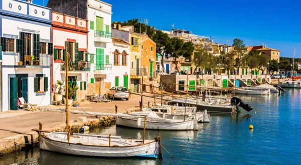 Bunte Häuserfront am Hafen, Boote im Wasser – ein idyllischer Urlaub auf Mallorca.