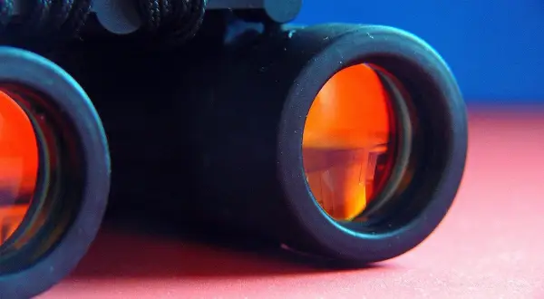 Primo piano di un binocolo nero con lenti arancioni, pronto per esplorare il mondo.
