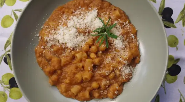 Pyszny makaron z ciecierzycy w sosie pomidorowym, posypany parmezanem i gałązką rozmarynu.