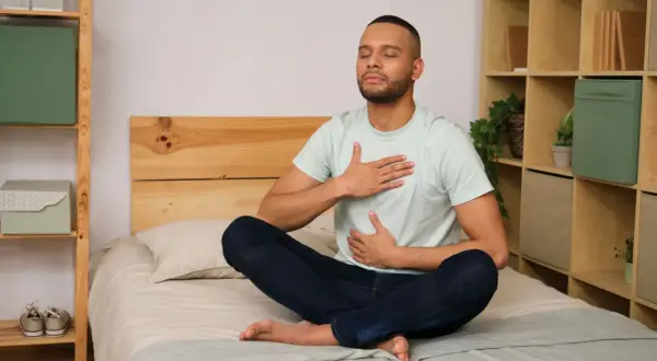 Man meditating on bed, practicing a breathing exercise to fall asleep in 60 seconds.